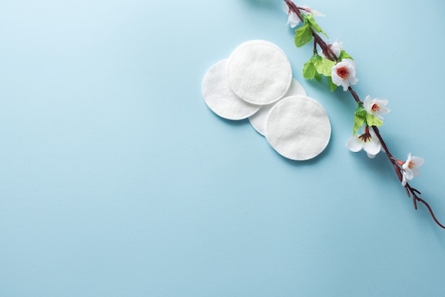 Almohadillas de algodón para quitar el maquillaje con flores blancas sobre el fondo azul flatlay