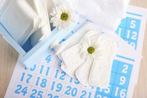 Almohadillas sanitarias en caja y almohadillas sanitarias y flores blancas en calendario azul sobre fondo gris claro