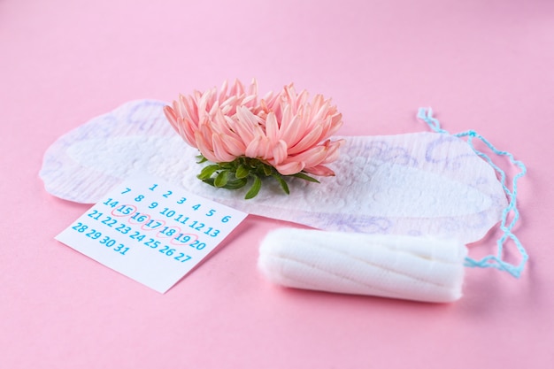 Almohadillas y tampones para la menstruación, calendario femenino y una flor rosa. cuidado de la higiene durante los días críticos. ciclo menstrual regular.