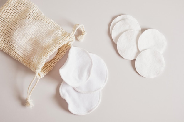 Almohadillas de tela y guata para limpiar la piel del maquillaje y bolsa de malla para guardarlas sobre un fondo beige