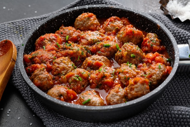 Almôndegas com molho de tomate servidas na frigideira em fundo escuro.