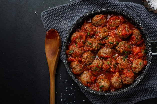 Almôndegas com molho de tomate servidas na frigideira em fundo escuro.