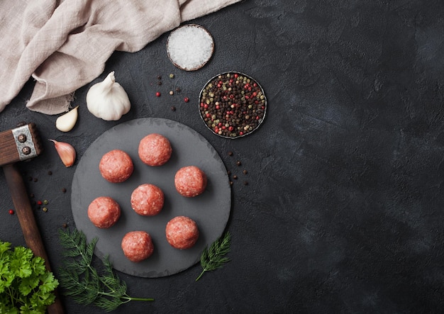 Almôndegas de carne picada fresca crua na placa redonda com sal de pimenta e alho em fundo preto com salsa e martelo de madeira