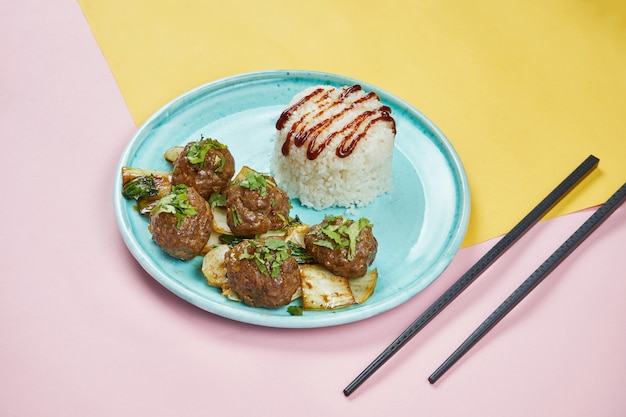 Almôndegas de estilo asiático com molho teriyaki, repolho frito e arroz em uma placa azul na superfície da cor. feche acima, copie o espaço para texto