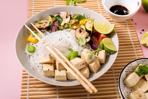 Almuerzo asiático vegano con fideos de arroz, tofu y verduras, comida tradicional china o vietnamita con palillos, vista superior