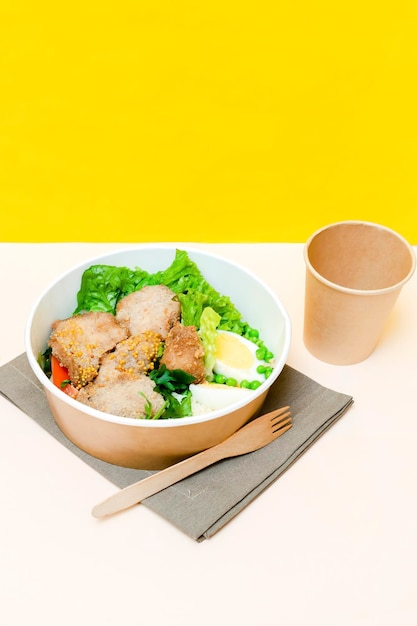 Almuerzo de comida saludable en cartón de papel kraft caja ecológica recipiente desechable recipiente de embalaje taza sobre fondo amarillo huevos de gallina verdes Entrega para llevar protección del medio ambiente vertical