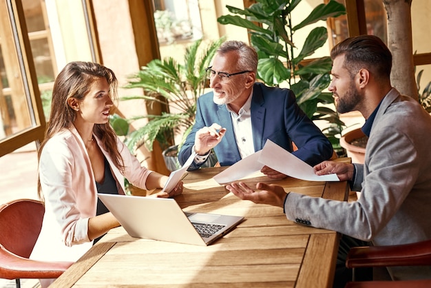 Almuerzo de negocios tres personas en el restaurante sentados a la mesa discutiendo el proyecto de trabajo en equipo alegre