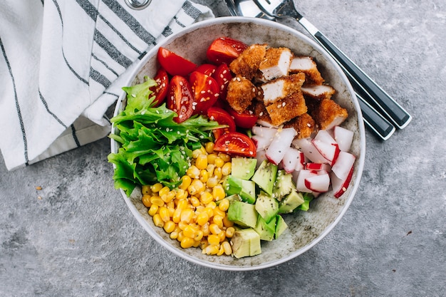 Almuerzo saludable Biddha bowl. Ensalada de verduras, aguacate, pollo, tomate, rábano, maíz, hojas verdes.