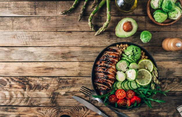 Almuerzo saludable en un tazón de Buda con pollo a la parrilla, rúcula, aguacate, coles de Bruselas, tomate, pepino y garbanzos.