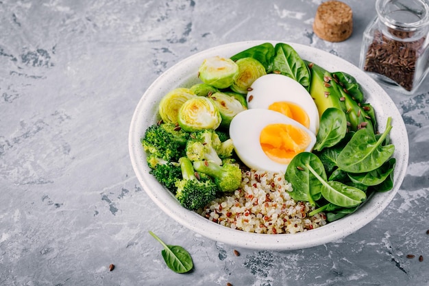 Almuerzo de tazón de Buda vegetariano verde saludable con huevos, quinua, espinacas, aguacate, coles de Bruselas a la parrilla y brócoli con semillas de lino sobre fondo gris oscuro