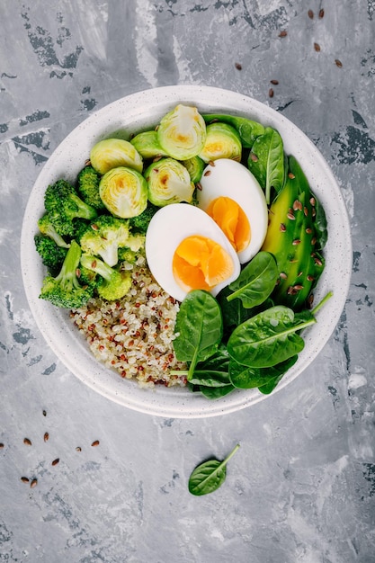 Almuerzo de tazón de Buda vegetariano verde saludable con huevos, quinua, espinacas, aguacate, coles de Bruselas a la parrilla y brócoli sobre fondo gris oscuro Vista superior