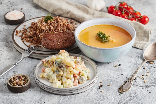 Almuerzo en tazón y platos con tenedor y cuchara, paño de cocina y tomates sobre fondo de mármol claro