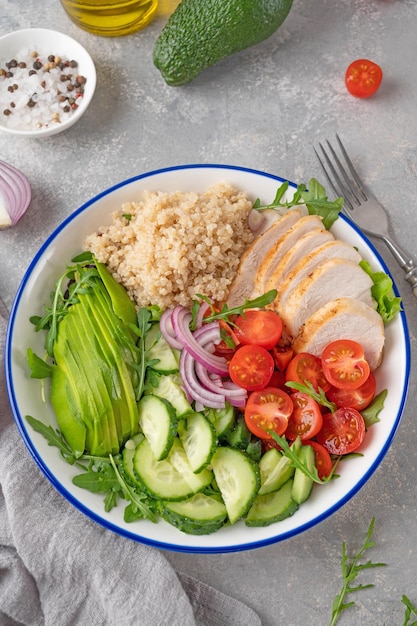 Almuerzo de tazón saludable con pollo a la parrilla, quinua, aguacate, tomates, pepinos y rúcula fresca