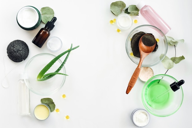 Aloe Vera Blätter, schwarzes Tonpulver, Eukalyptusblätter, Vitamin C, Blütenextrakt, Flaschen mit Seren, Stärkungsmittel, Gläser mit Sahne und Gel auf weißem Hintergrund. Das Konzept der Hautpflege, ihre Flüssigkeitszufuhr