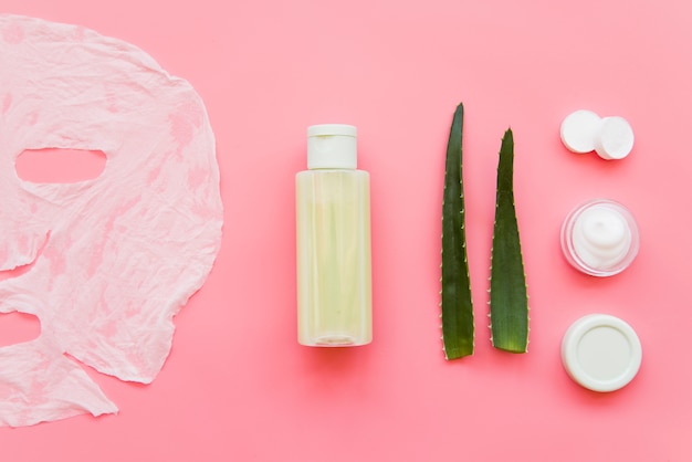 Aloe Vera creme hidratante para a pele; loção e máscara de folha de papel no pano de fundo rosa