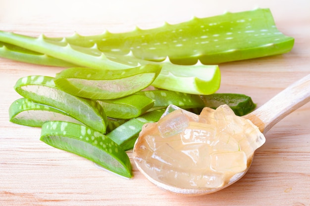 Aloe Vera schneidet frisches Blatt mit klarem Gelee in einem Löffel auf einem Holztisch