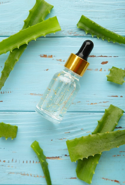 Aloe vera und ölflasche auf blauem holzhintergrund. vertikales foto.