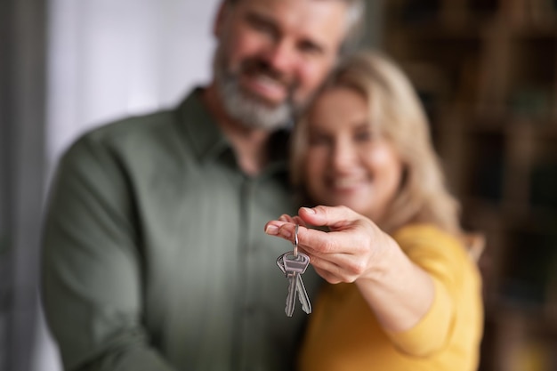 Alojamiento familiar Cónyuges felices de mediana edad posando con llaves de casa en las manos