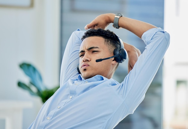 Alongamento cansado e homem no call center com estresse para atendimento ao cliente de telemarketing e consultoria de vendas Desconfortável preguiçoso e agente do sexo masculino em uma pausa para fadiga de esgotamento ou entediado no suporte técnico