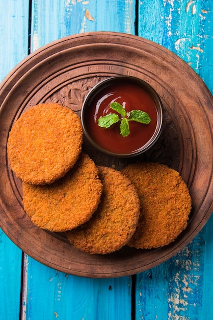 Aloo Tikki oder Patties oder Cutlet ist ein beliebter Snack oder Snack aus Indien, serviert mit Tomatenketchup oder Imli-Chutney über stimmungsvollem Hintergrund. Selektiver Fokus