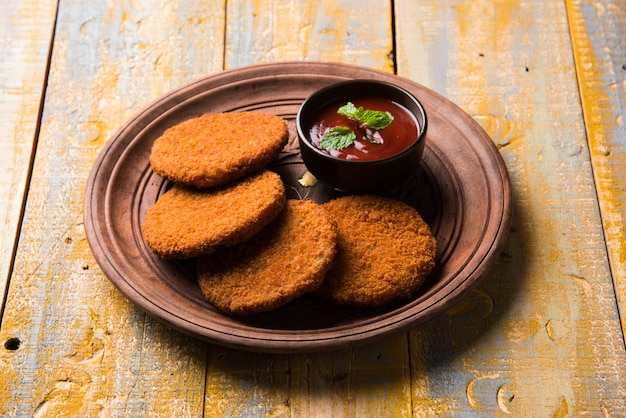 Aloo Tikki oder Patties oder Cutlet ist ein beliebter Snack oder Snack aus Indien, serviert mit Tomatenketchup oder Imli-Chutney über stimmungsvollem Hintergrund. Selektiver Fokus