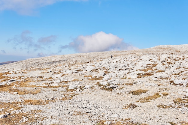 Alpenplateau bedeckt mit trockenem Gras und weißen Steinen und ein paar Reisende in der Ferne