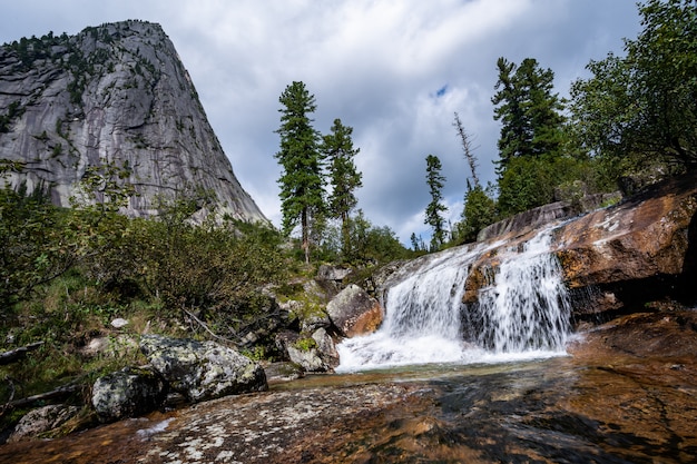 Alpiner Wasserfall im Gebirgswald unter blauem Himmel.