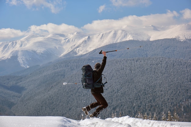 Foto alpinista bem-sucedida com mochila caminhando na encosta da montanha nevada num dia frio de inverno.