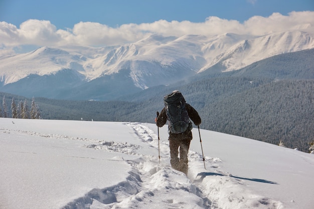 Alpinista com mochila caminhando na encosta da montanha nevada num dia frio de inverno.