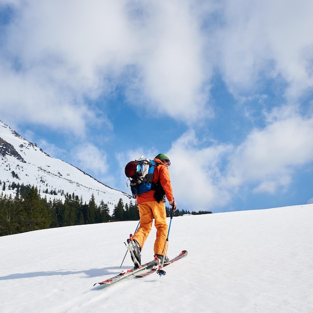 Alpinista de esqui subindo ao longo do cume nevado com os esquis na mochila