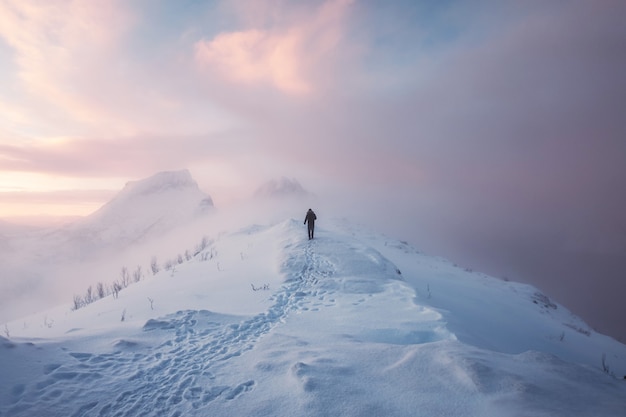 Alpinista de homem andando com pegada na montanha de neve e céu colorido na nevasca ao nascer do sol.