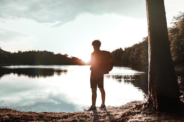 Alpinista de homem de sucesso caminhando no lago ao nascer do sol Jovem olha o horizonte satisfeito Conceito de destino de viagem de descoberta