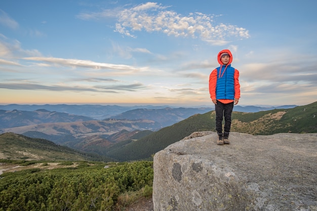 Alpinista de menino jovem criança em pé nas montanhas, apreciando a vista da paisagem de montanha incrível.