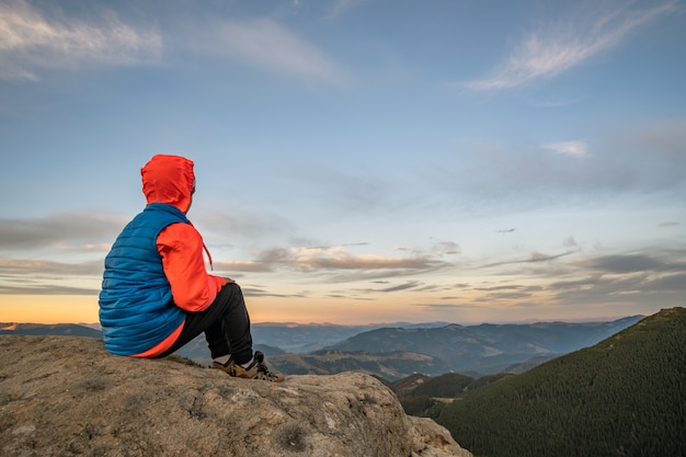 Alpinista de menino jovem criança sentada nas montanhas, apreciando a vista da paisagem de montanha incrível.