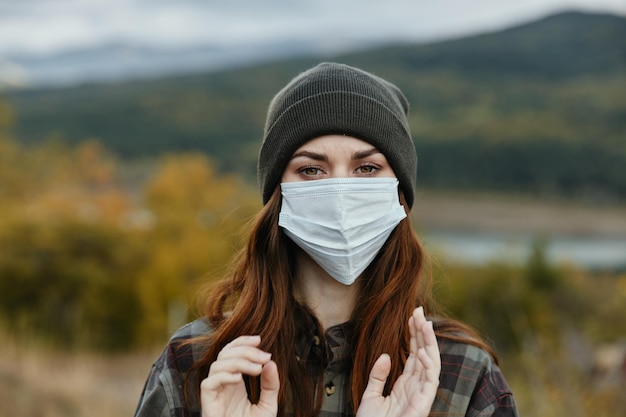 Alpinista de mulher com uma máscara médica e um chapéu quente na natureza na floresta no prado