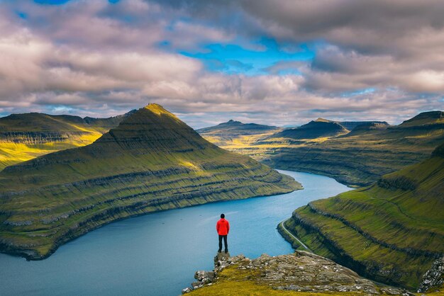 Alpinista desfruta de vistas sobre fiordes de uma montanha perto de funningur nas ilhas faroe