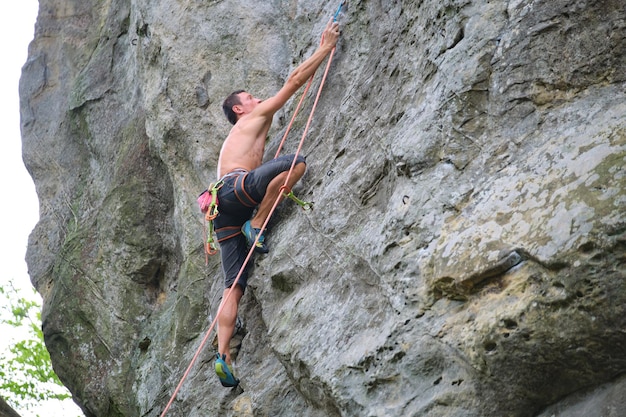Alpinista determinado escalando a parede íngreme da montanha rochosa Desportista superando a rota difícil Envolvendo-se em esportes radicais e conceito de hobby de escalada