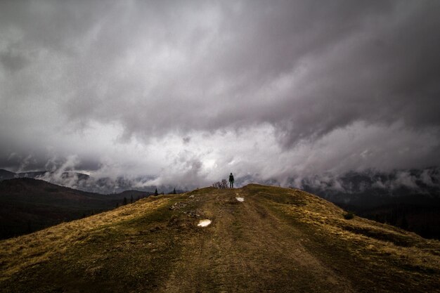 Alpinista em pé na foto de paisagem de colina de grama seca