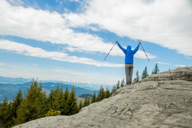 Un alpinista está en lo alto de las montañas contra el cielo, celebrando la victoria, levantando las manos.