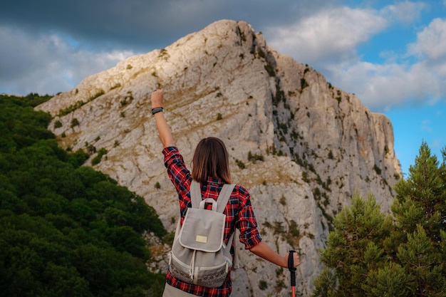 Alpinista feminina apta com mochila em pé em um cume de montanha rochosa