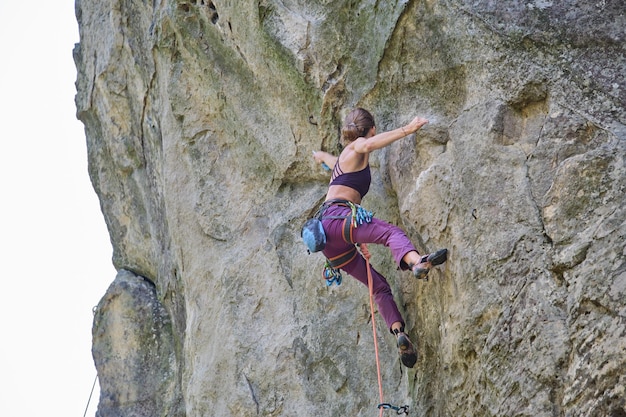 Alpinista feminina forte escalando a parede íngreme da montanha rochosa Desportista superando a rota difícil Envolvendo-se no conceito de hobby de esportes radicais