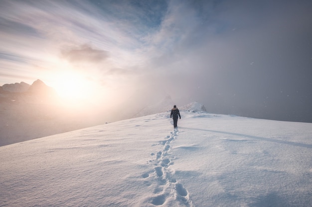 Alpinista hombre caminando con huella de nieve en cresta pico