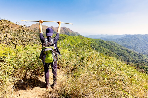 Foto alpinista, levantando os braços e segurando a vara de madeira no topo de uma montanha