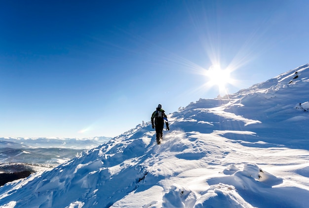 Un alpinista masculino caminando cuesta arriba sobre un glaciar. Alpinista llega a la cima de una montaña nevada en un soleado día de invierno.