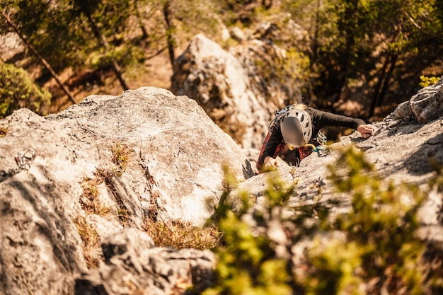 Alpinista usando equipamento de escalada Praticando escalada em uma parede de montanha de rocha Esportes de escalada e conceito de boulder alpinista sobe em uma parede rochosa