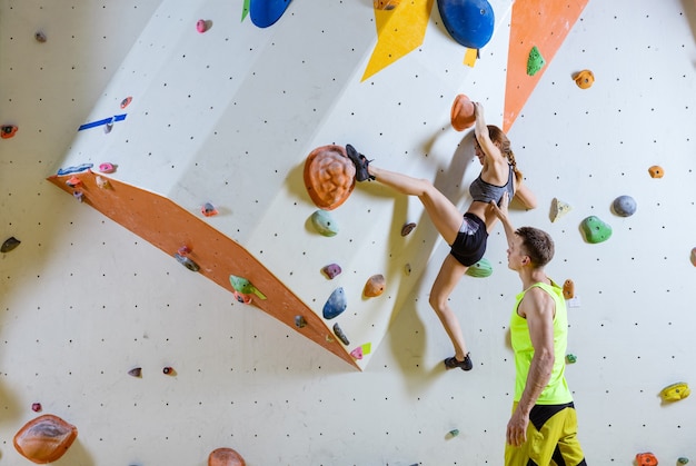 Alpinistas no ginásio de escalada. Problema de escalada com pedras (rota), instrutor masculino protegendo-a.