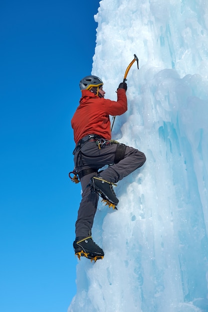 Alpinistmann mit der Eiswerkzeugaxt, die eine große Wand des Eises klettert. Sport im Freien Porträt.