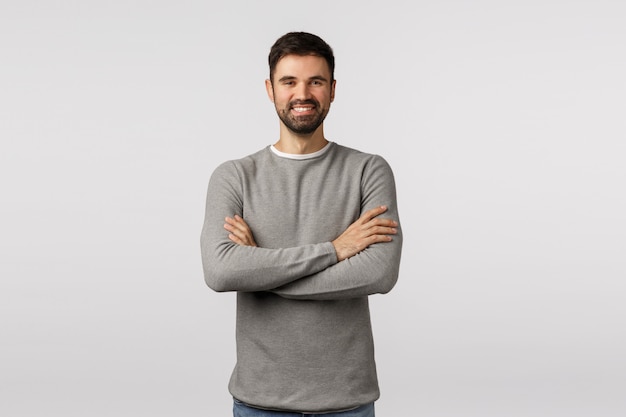 Alquiler, empleo y concepto de empresa. Alegre guapo hombre barbudo caucásico con suéter gris, pecho cruzado, sonriendo complacido y seguro de sí mismo, hora entrevistando a un empleado