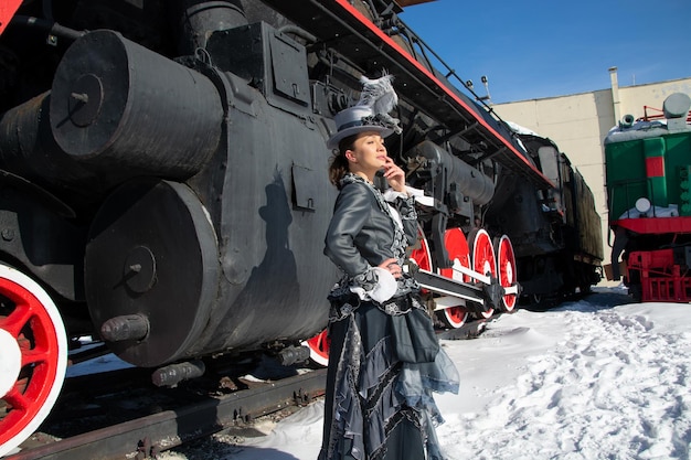 Als Adlige des 19. Jahrhunderts gekleidetes Mädchen in der Nähe einer Dampflokomotive Russischer Winter