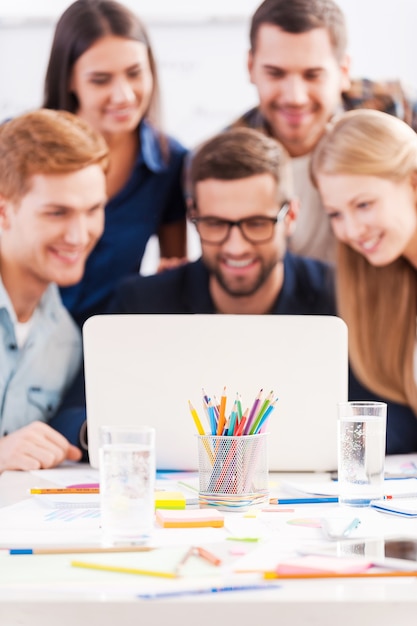 Als team arbeiten. gruppe fröhlicher geschäftsleute in eleganter freizeitkleidung, die zusammen den laptop betrachten und lächeln